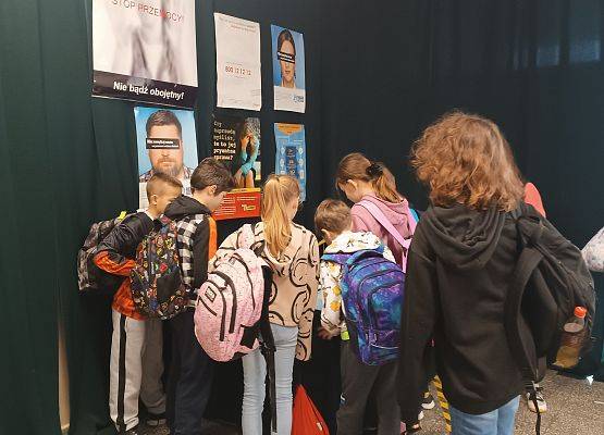 Uczniowie stoją w holu przy kąciku informacyjnym