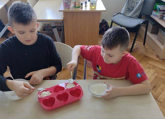 dwaj chłopcy przekładają masę z miseczki do foremek