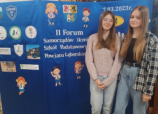 uczennice stoją na tle dekoracji na temat II forum