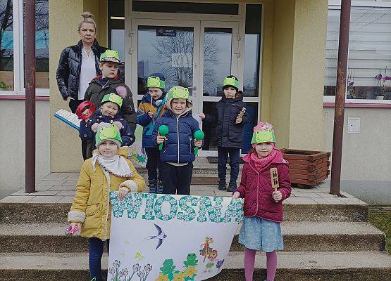 dzieci wychodzą z przedszkola i trzymają plakat z napisem wiosna