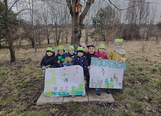 dzieci stoją w sadzie i prezentują wiosenne plakaty