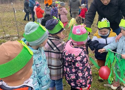 dzieci z nauczycielką sadzą drzewko w sadzie