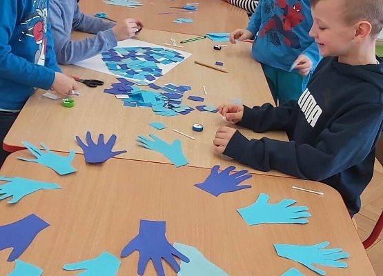 dzieci wycinają z papieru niebieskie dłonie