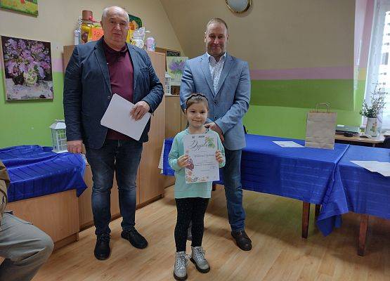 dziewczynka trzyma dyplom , za nią stoją dyrektor Gminnego Ośrodka Kultury w Nowej Wsi Lęborskiej oraz radny