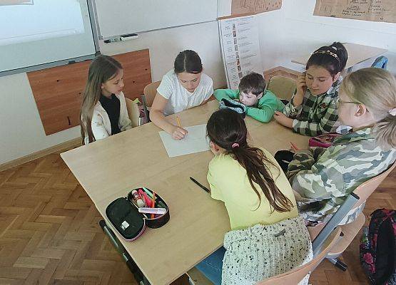uczniowie siedzą przy stoliku i pracują w grupie