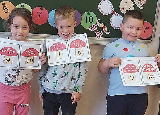 dzieci stoją przy tablicy i prezentują swoje prace