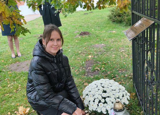 uczennica składa kwiaty i znicz pod dębem katyńskim