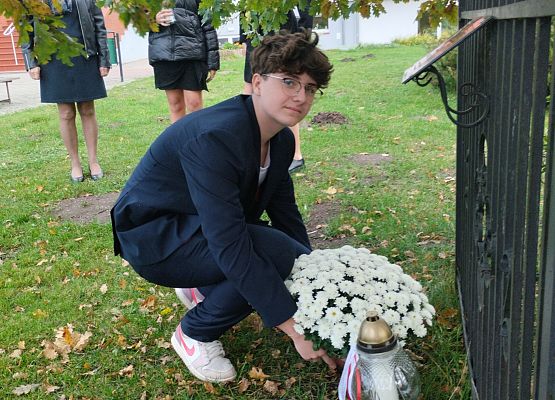 uczeń składa kwiaty i znicz pod dębem katyńskim