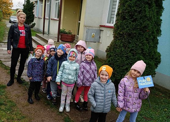 dzieci przed wejściem do przedszkola trzymają tabliczkę z napisem