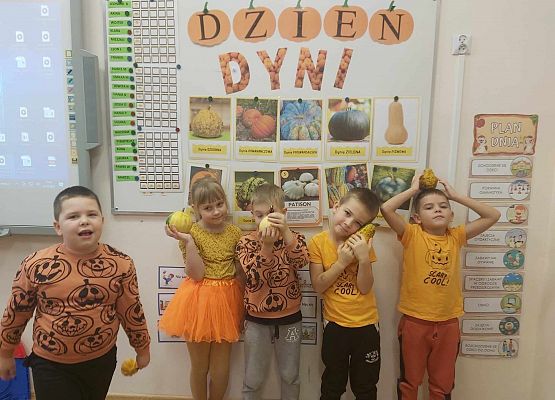 Dzieci stoją pod tablicą i trzymają dynie