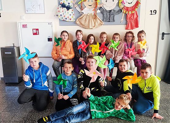 dzieci na tle szkolnej gazetki prezentują wykonane wiatraczki