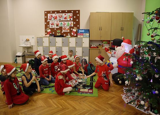 uczniowie siedzą na dywanie i odbierają paczki