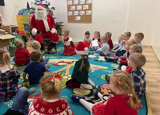 dzieci siedzą na podłodze i słuchają Mikołaja