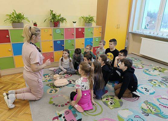 uczniowie siedzą na dywanie i słuchają pani