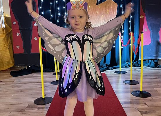 dziewczynka w stroju motyla stoi na czerwonym dywanie