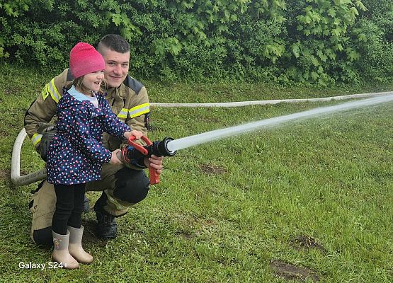 dziewczynka i strażak polewają wodą trawę