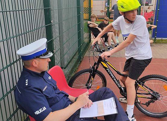 policjant wyjaśnia uczniowi zasady jazdy po miasteczku ruchu drogowego
