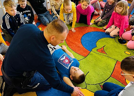 Policjant pokazuje dzieciom, jak ułożyć poszkodowanego w bezpiecznej pozycji