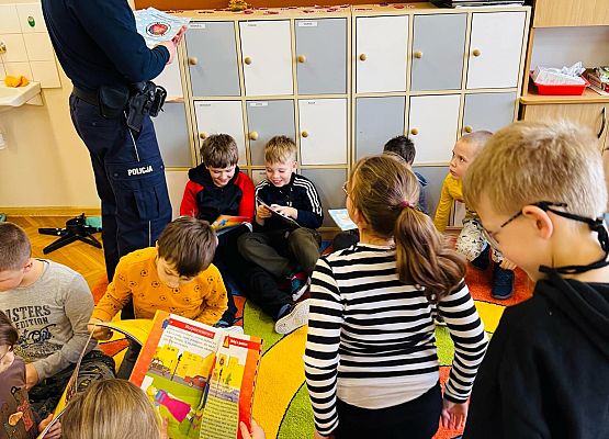 policjant rozdaje dzieciom książeczki