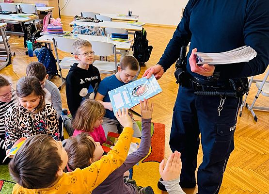 policjant rozdaje dzieciom książeczki