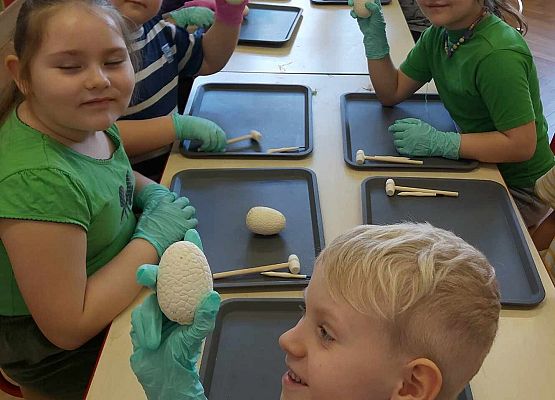 Dzieci siedzą przy stole i pokazują gipsowe jajka dinozaura