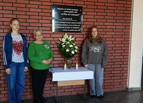 nauczycielka i uczennice przy tablicy pamięci Jana Pawła II