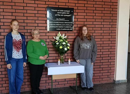 nauczycielka i uczennice przy tablicy pamięci Jana Pawła II