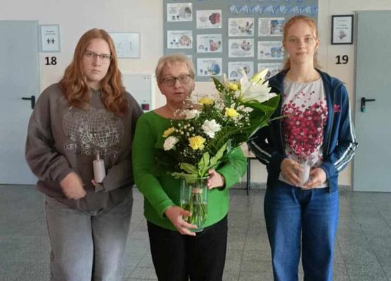 nauczycielka i uczennice niosą kwiaty i znicze