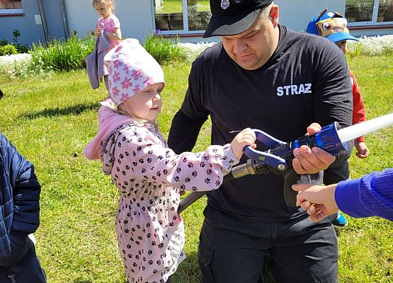 strażak z dziećmi podczas zajęć przed budynkiem szkoły