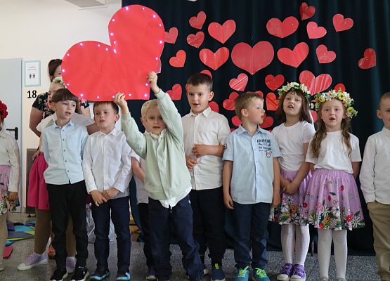 dzieci występują, chłopiec trzyma papierowe serce