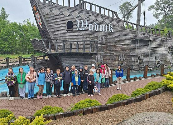 uczniowie stoją przed drewnianym statkiem