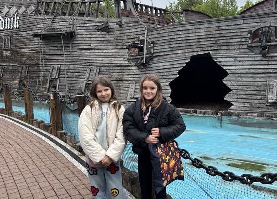 dziewczynki stoją przed drewnianym statkiem