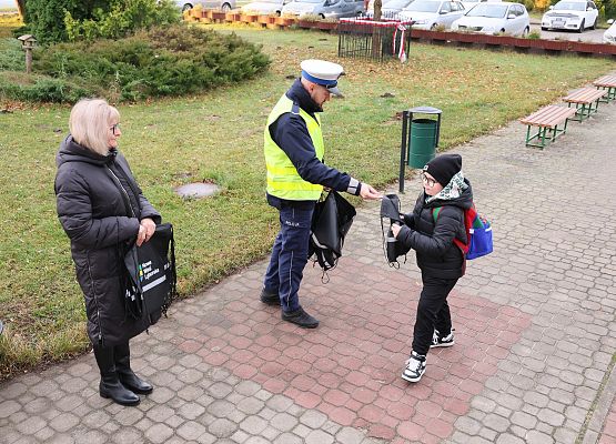 pani wicedyrektor i policjant rozdają dzieciom materiały odblaskowe