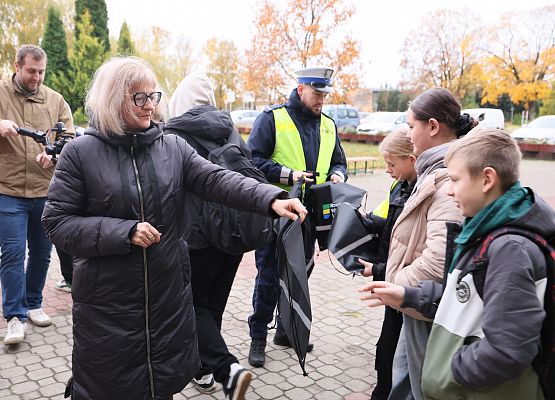 wicedyrektor i policjant rozdają dzieciom materiały odblaskowe