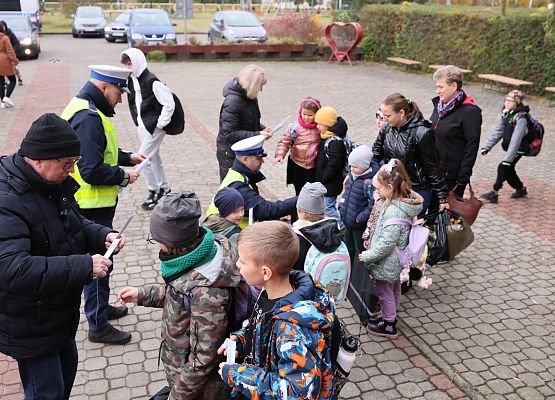 dyrektor i policjant  rozdają dzieciom materiały odblaskowe