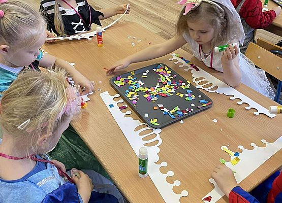 dzieci w kolorowych strojach wykonują zadania przy stolikach