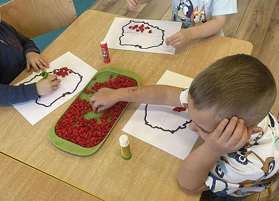 Dzieci wyklejają z bibuły szablon Polski