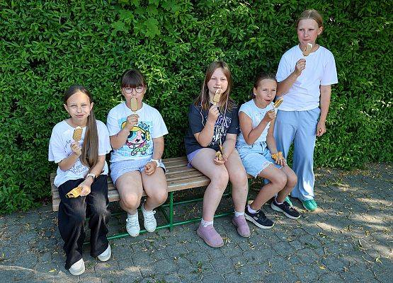 dzieci siedzą na łąwce i jedzą lody